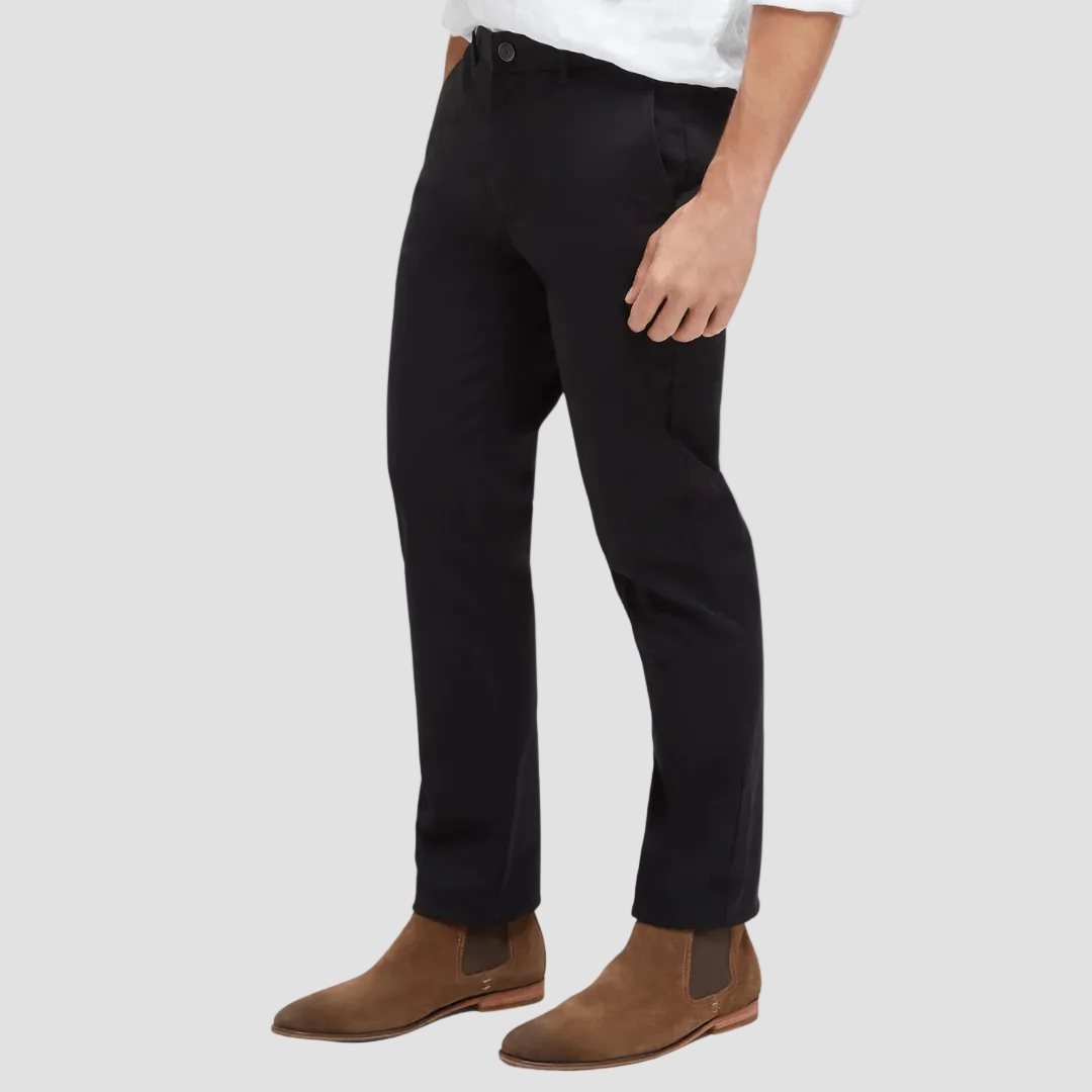 A man wearing black tailored fit chino pants with a white shirt and brown boots.
