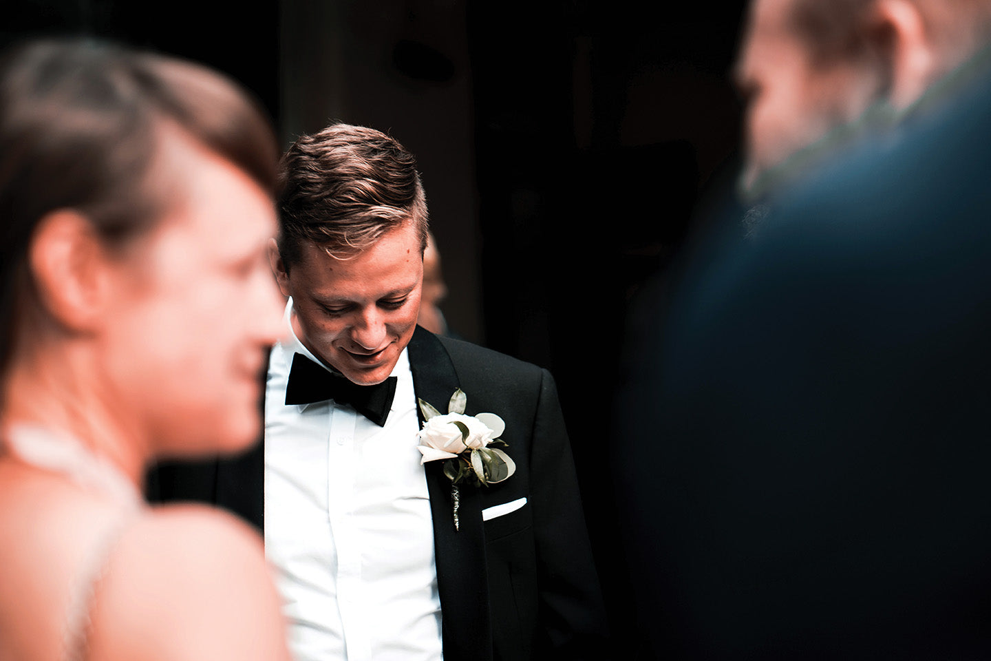 a groom stands waiting for the bride to arrive he wears a black wedding tuxedo a white dinner shirt and a black bow tie