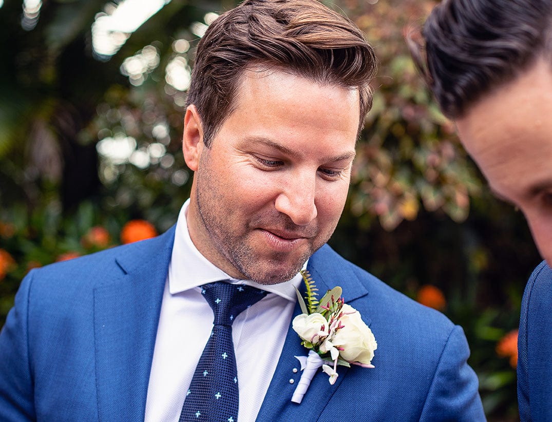 a groom waits for his bride on his wedding day he is wearing a cobolt blue formal suit with a white shirt and spotted blue tie.