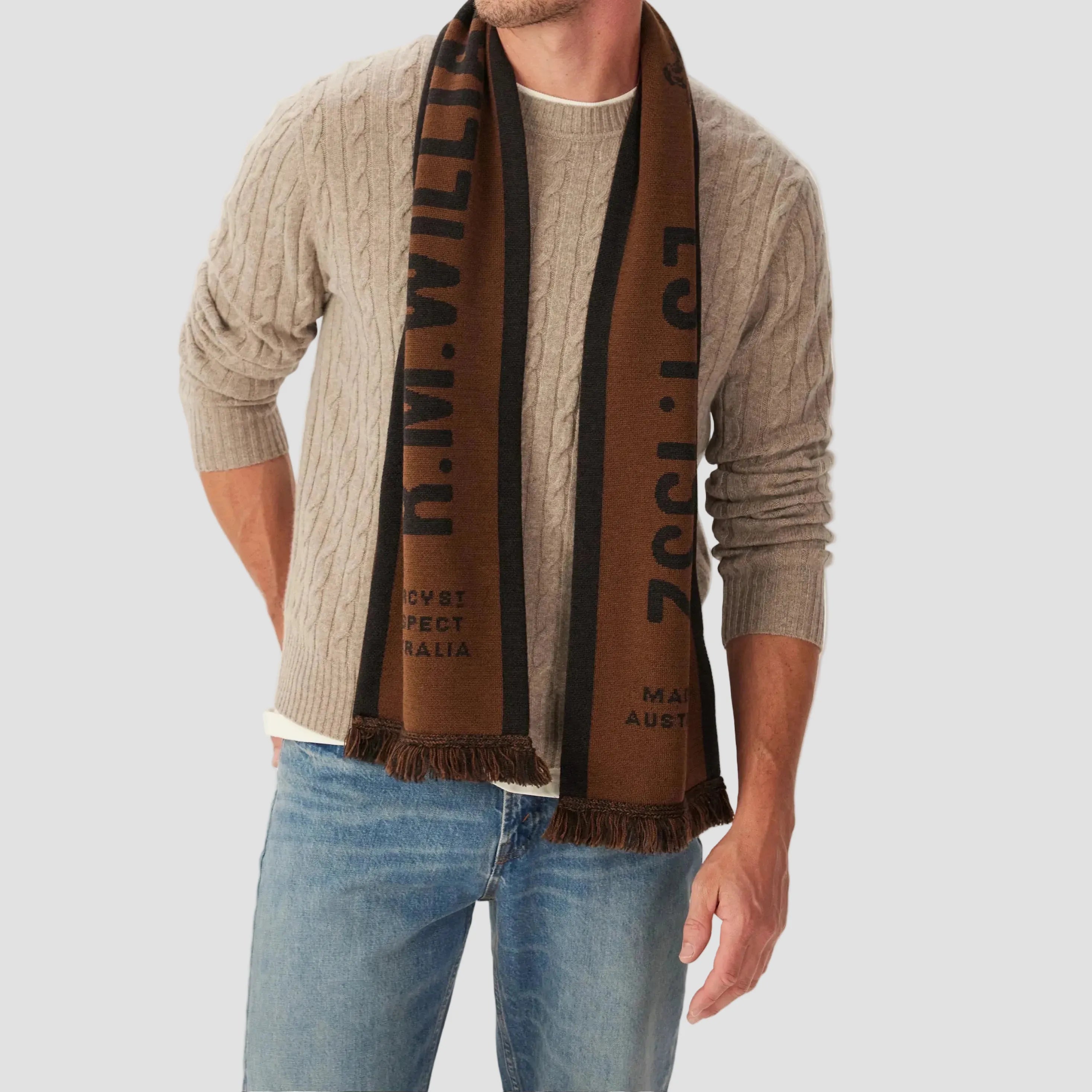 Man wearing a brown scarf with text, beige sweater, and blue jeans on a white background