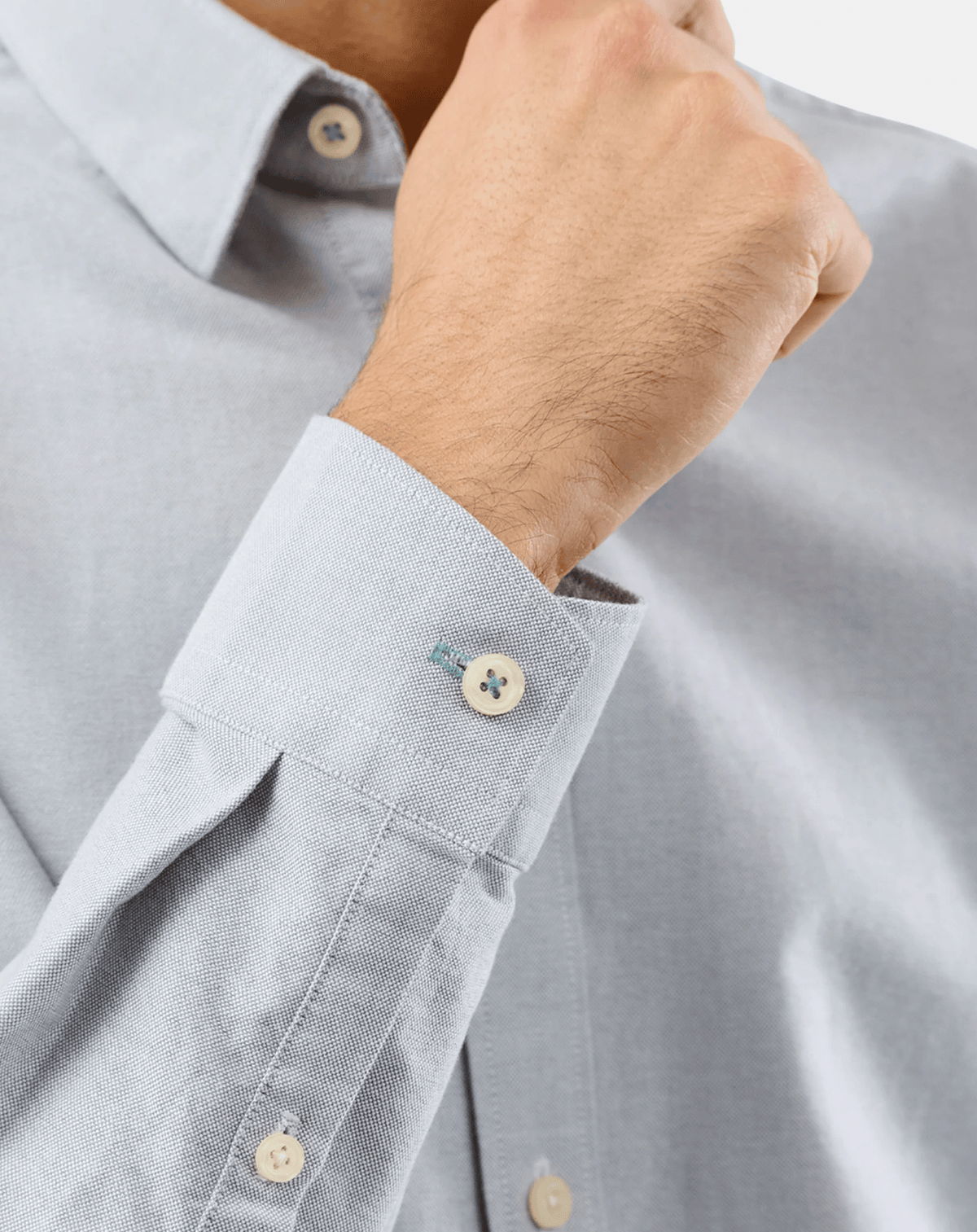 Close-up of a person wearing a light blue textured dress shirt, showing the buttoned collar and the cuff with a cream-colored button.