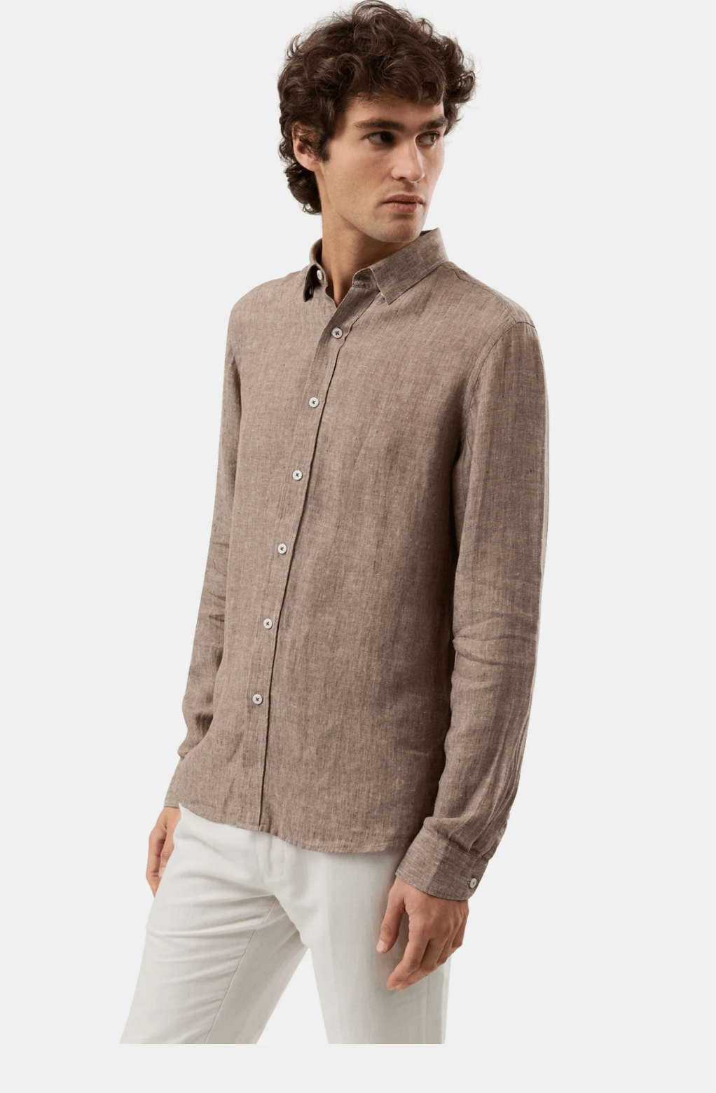 A man wearing a light brown linen button-down shirt and white trousers, photographed against a clean light gray studio background.