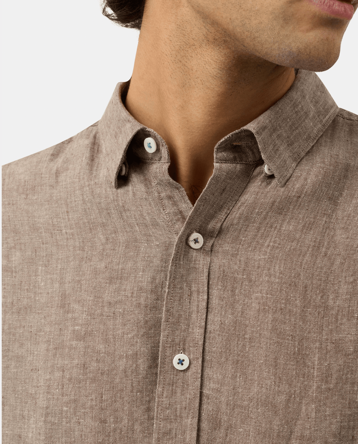 Close-up of a man wearing a textured brown linen button-down shirt with white buttons.