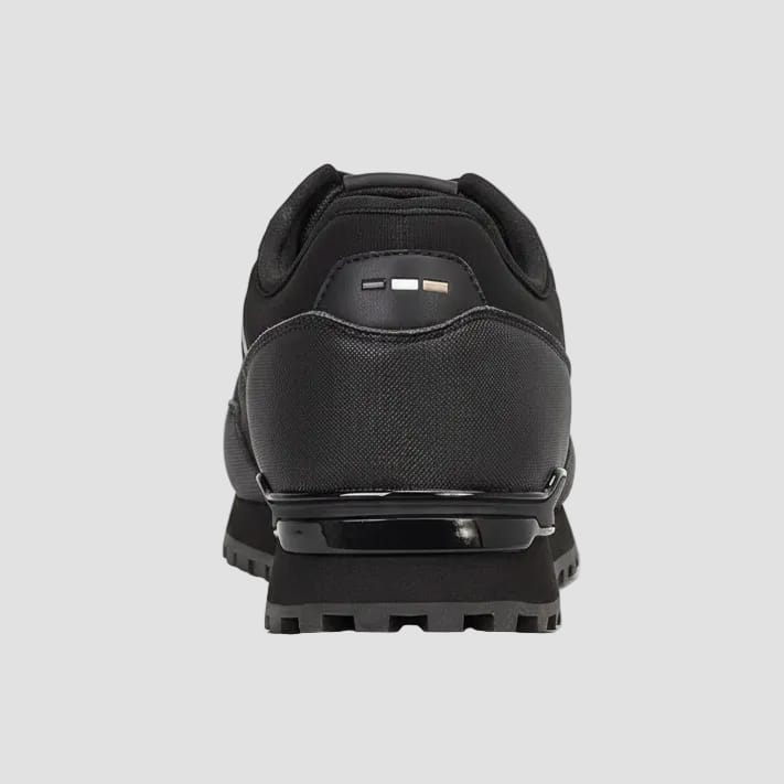 Close-up rear view of a black athletic shoe with textured synthetic and mesh panels, a glossy black midsole section, and three small color blocks on the heel tab against a white background.