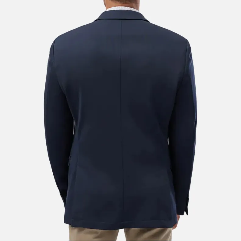 A man viewed from the back wearing a navy blue blazer over a white collared shirt and khaki trousers, set against a plain light gray studio background.