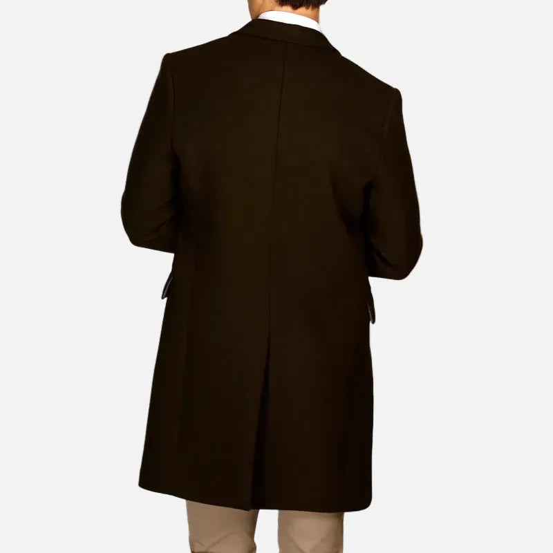 A man viewed from behind wearing a dark brown overcoat, beige trousers, and a white collared shirt, set against a solid light gray background.