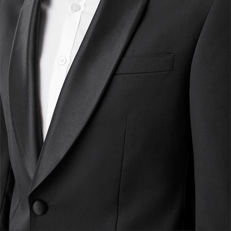Close-up of a man wearing a black shawl-lapel suit jacket over a white collared shirt, cropped from the lower face to the chest on a plain light background.