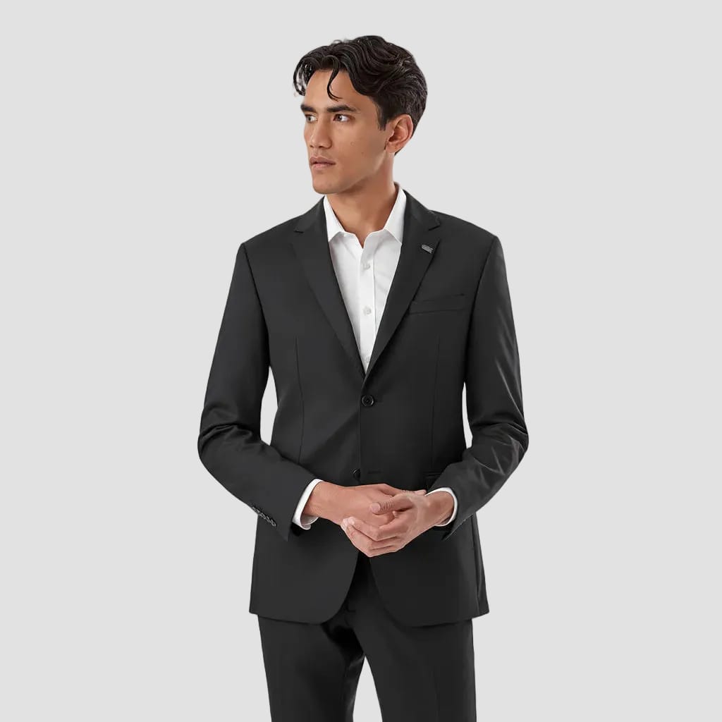 A man wearing a black slim-fit suit jacket and matching trousers over a white dress shirt, standing against a plain white background.