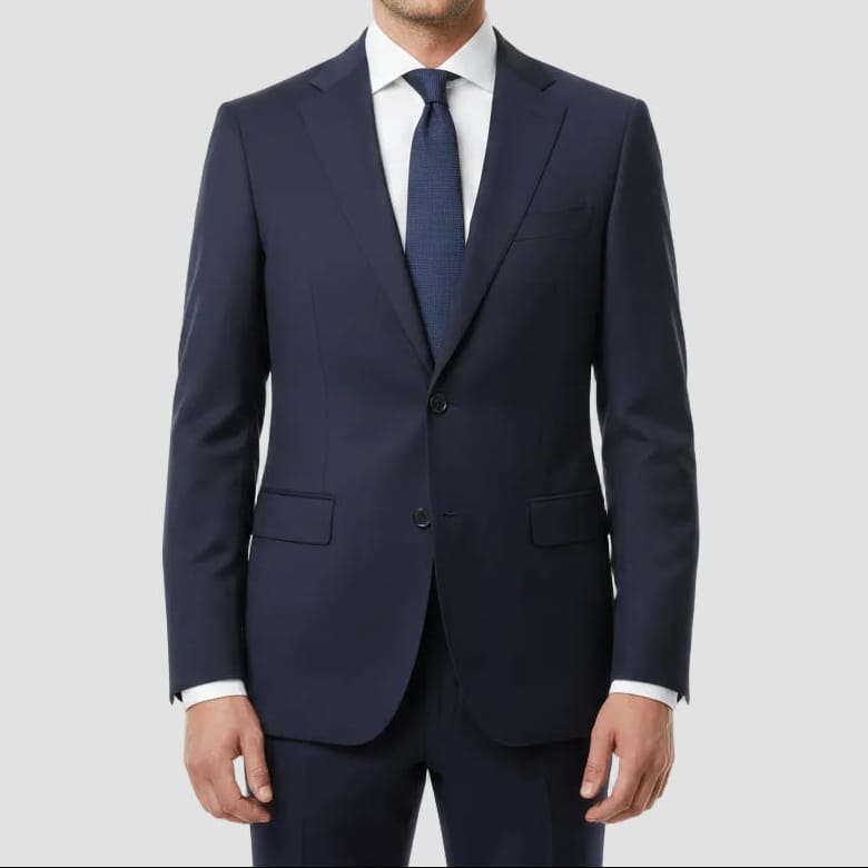 Man wearing a navy suit with a white shirt and blue tie on a light gray background