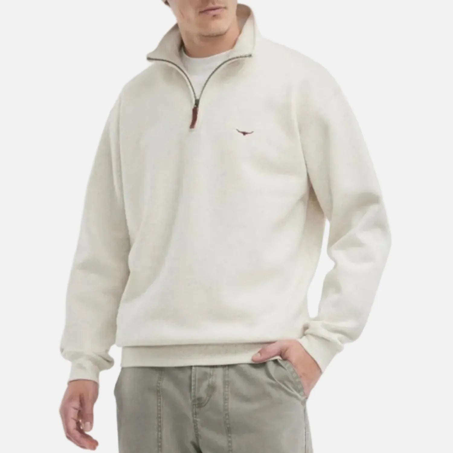 A man wearing a cream-colored quarter-zip sweatshirt with a small embroidered logo on the left chest, paired with light gray pants, against a plain white background.