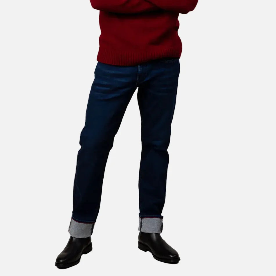 Man wearing a red sweater and blue jeans standing against a beige background