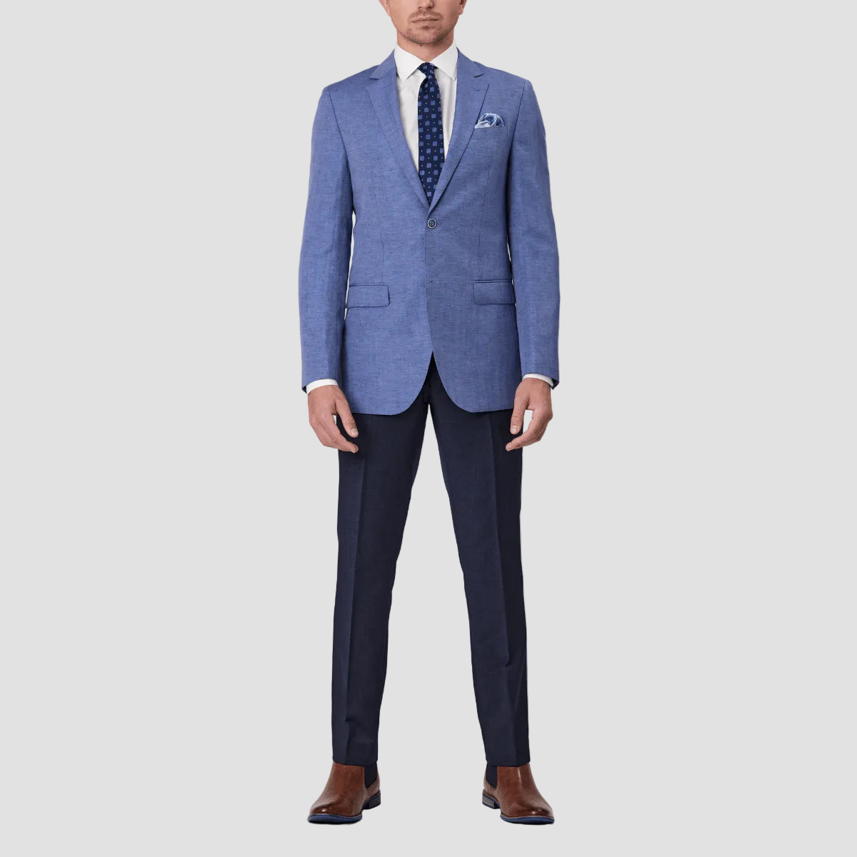 A man wearing a sky blue linen blend sports jacket by Savile Row with a notched lapel, paired with a white shirt, blue patterned tie, blue trousers, and brown leather shoes.