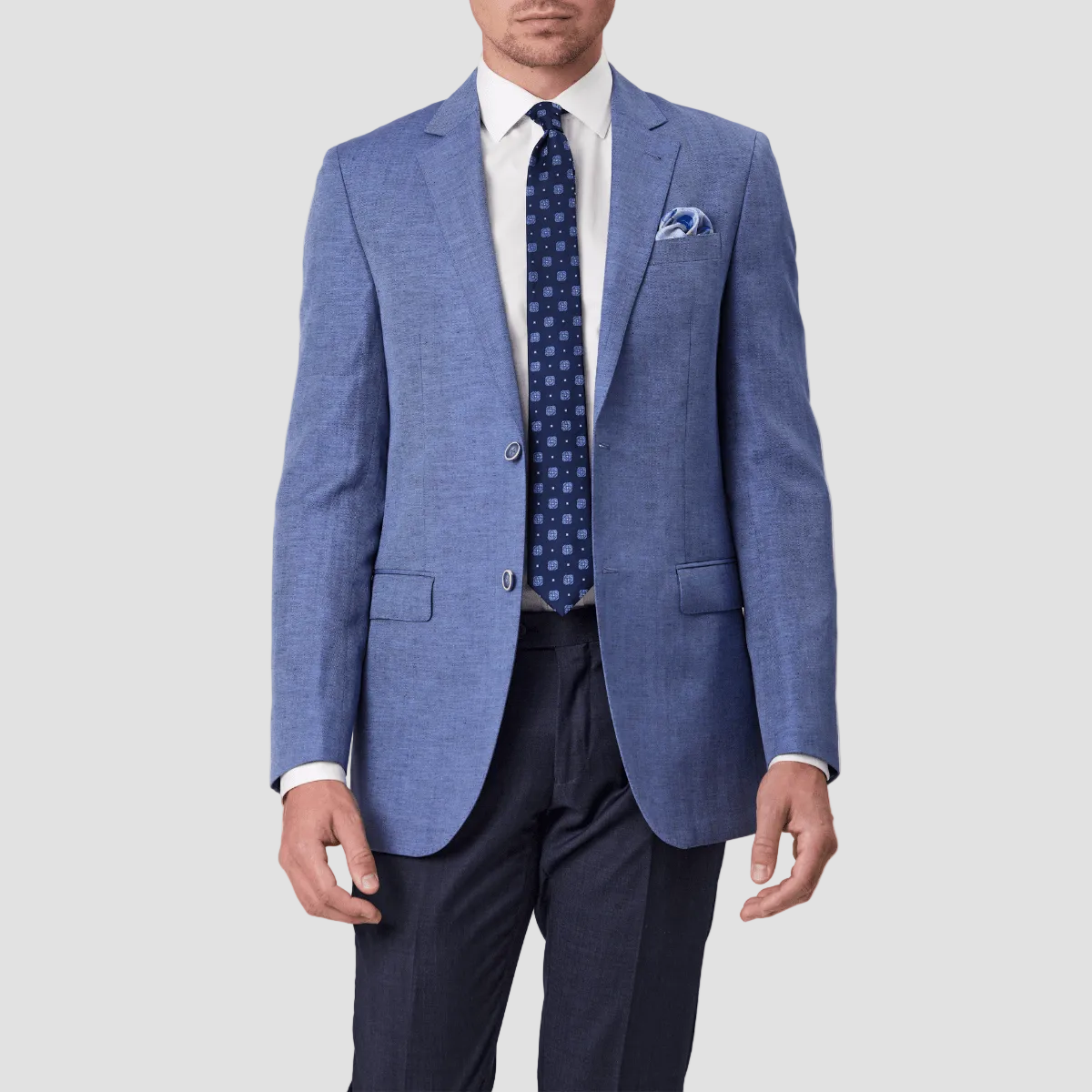 A man wearing a sky blue linen blend sports jacket by Savile Row with a notched lapel, paired with a white shirt, blue patterned tie and blue pants.