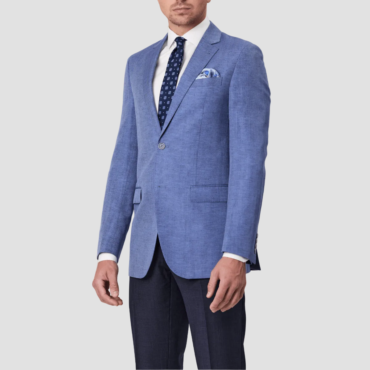 A man wearing a sky blue linen blend sports jacket by Savile Row with a notched lapel, paired with a white shirt, blue patterned tie and blue pants.