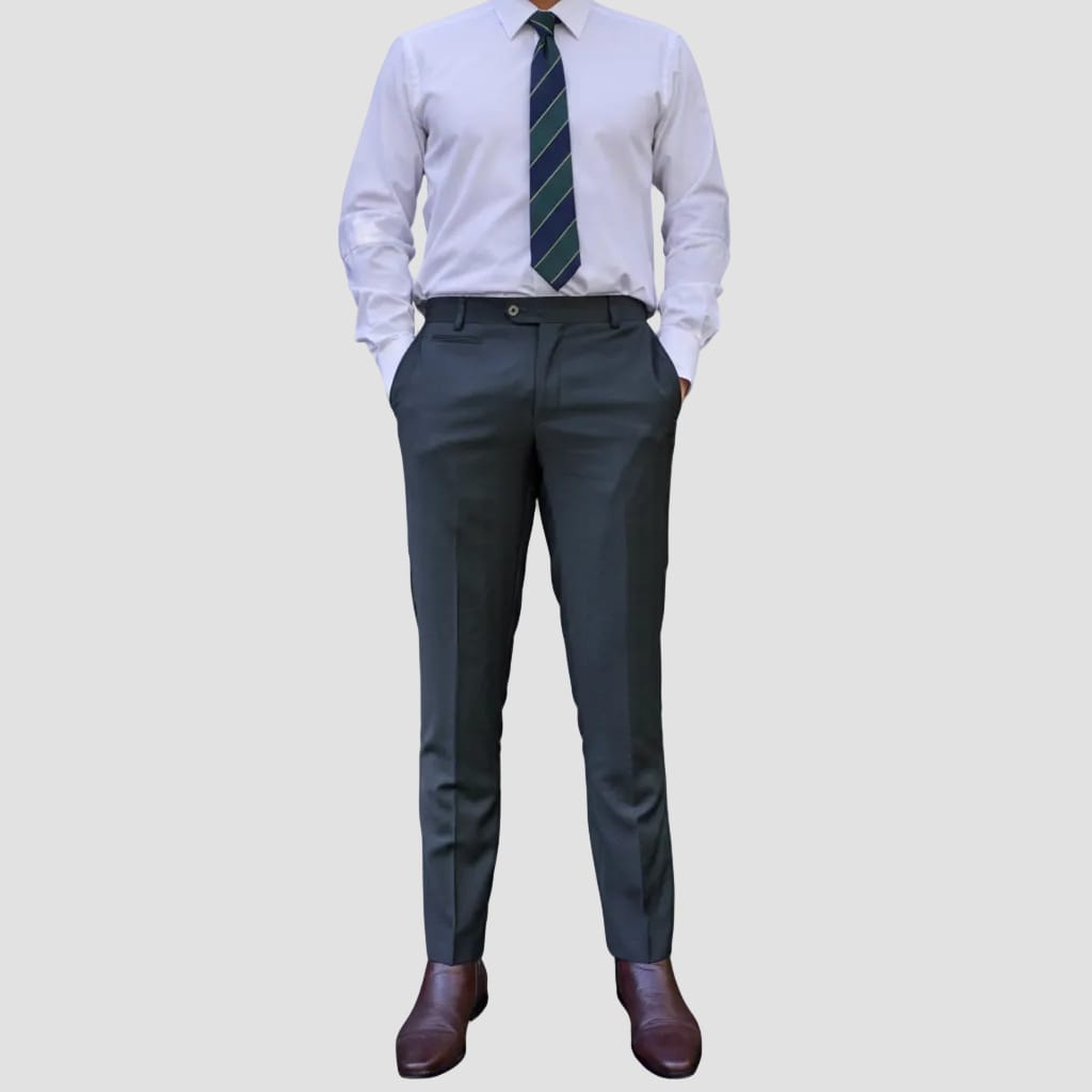 A person wearing slim-fit charcoal gray dress pants, styled with a white dress shirt, a green and navy striped tie, and dark brown leather dress shoes, shown from the waist down against a solid light gray background.