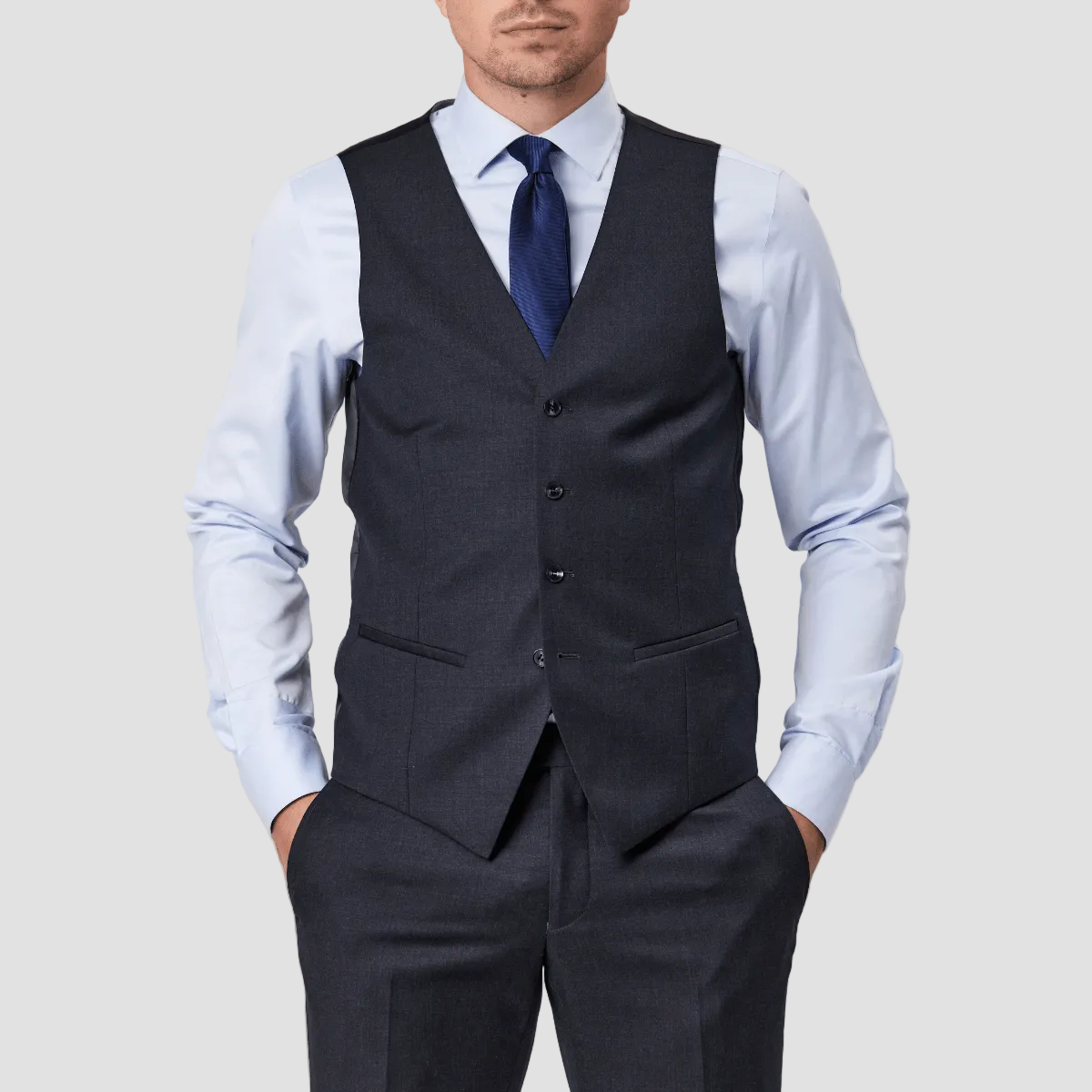 Tailored fit charcoal wool vest by Savile Row with a four-button front, paired with matching trousers and a light blue shirt and a blue tie.