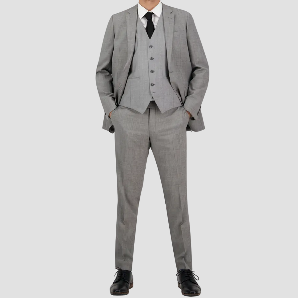 A man standing, wearing a chrome grey tailored fit suit with a notched lapel and trousers, paired with a gray tie and black shoes.