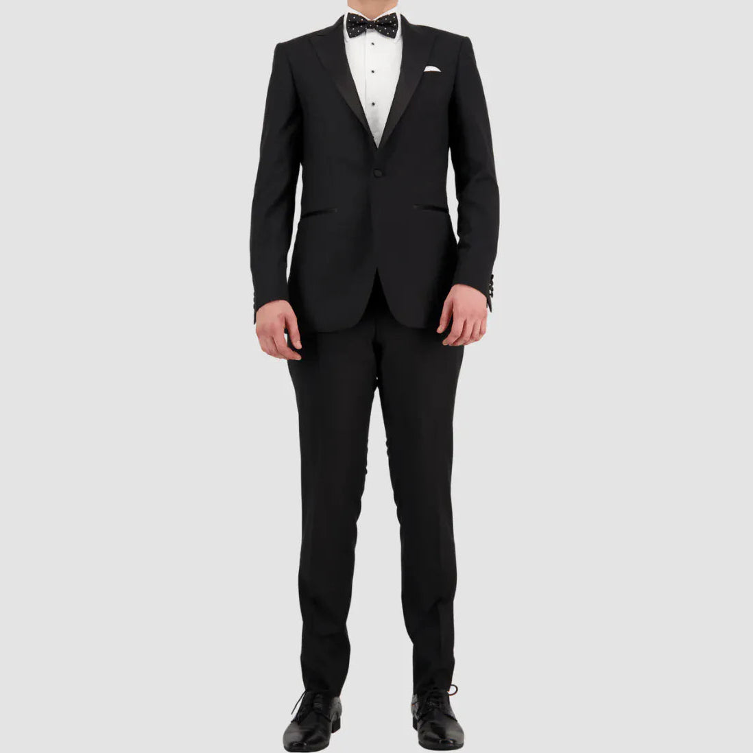 Man wearing a black tuxedo with a white shirt and bow tie on a light gray background