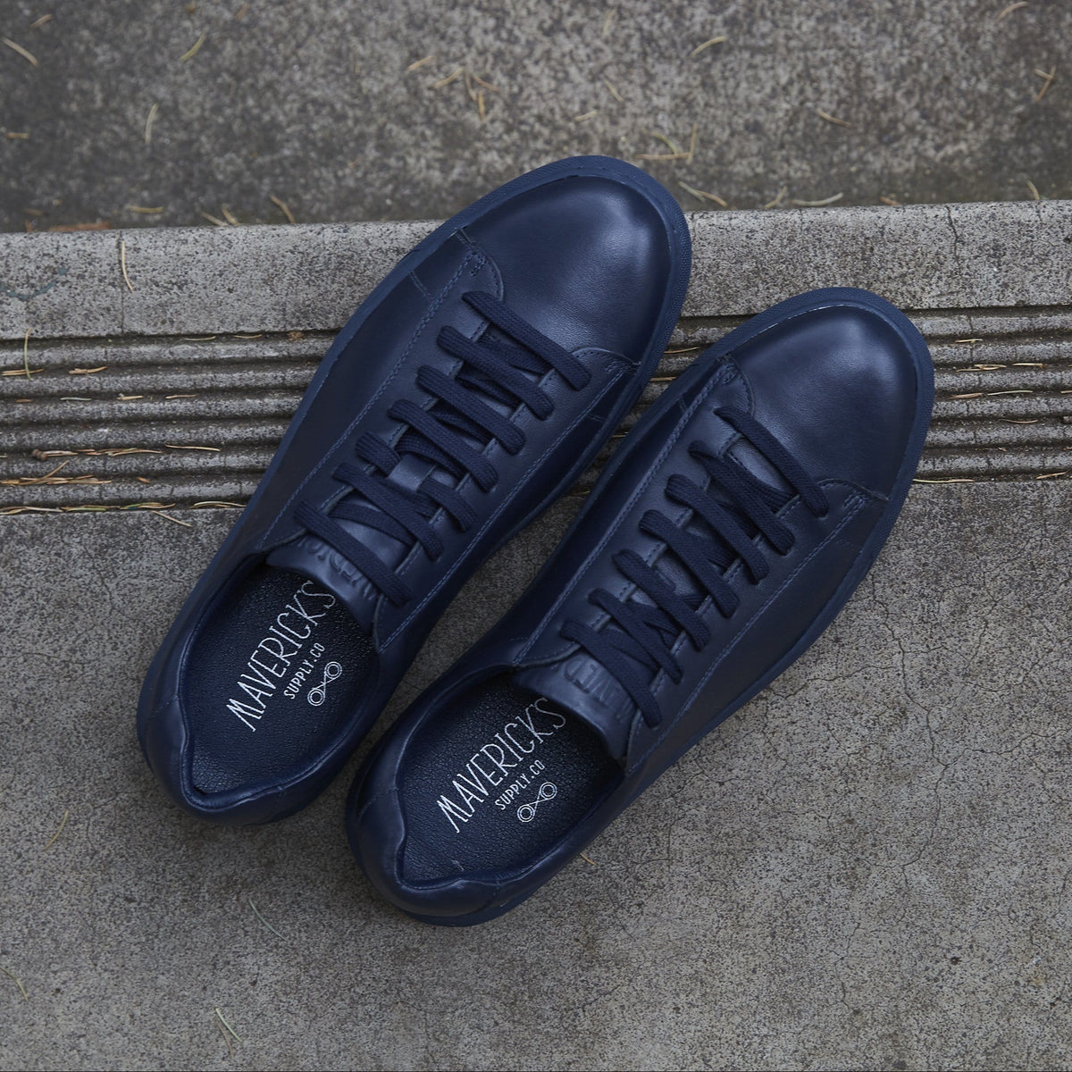 a top view of the mavericks mens leather sneakers in navy blue sitting on a concrete step