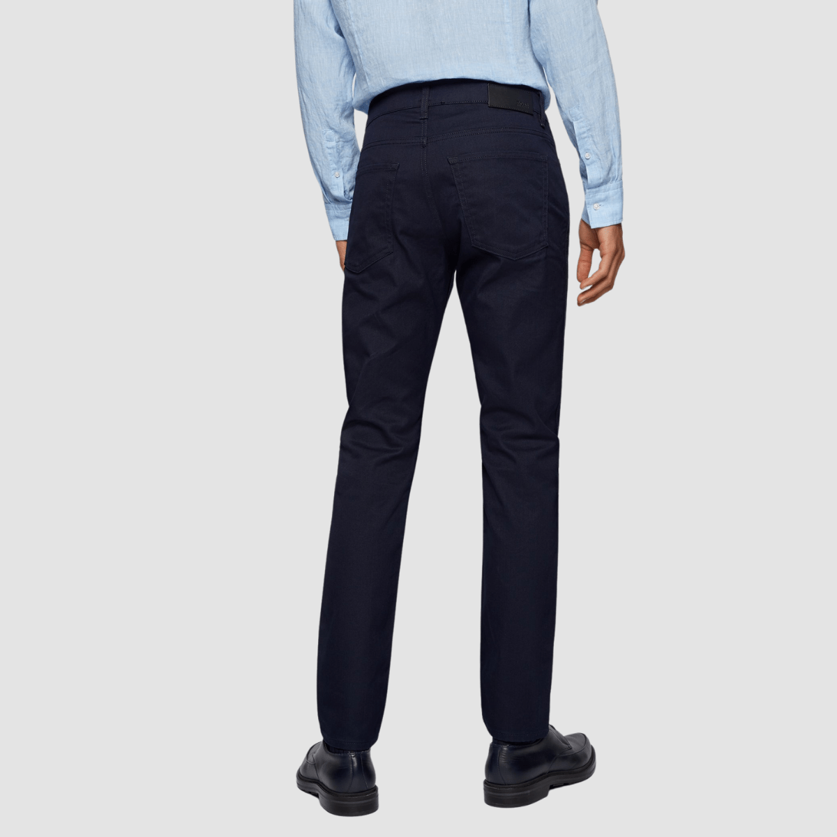 back of a man wearing dark slim fit hugo boss jeans with black leather shows and a light blue shirt tucked in
