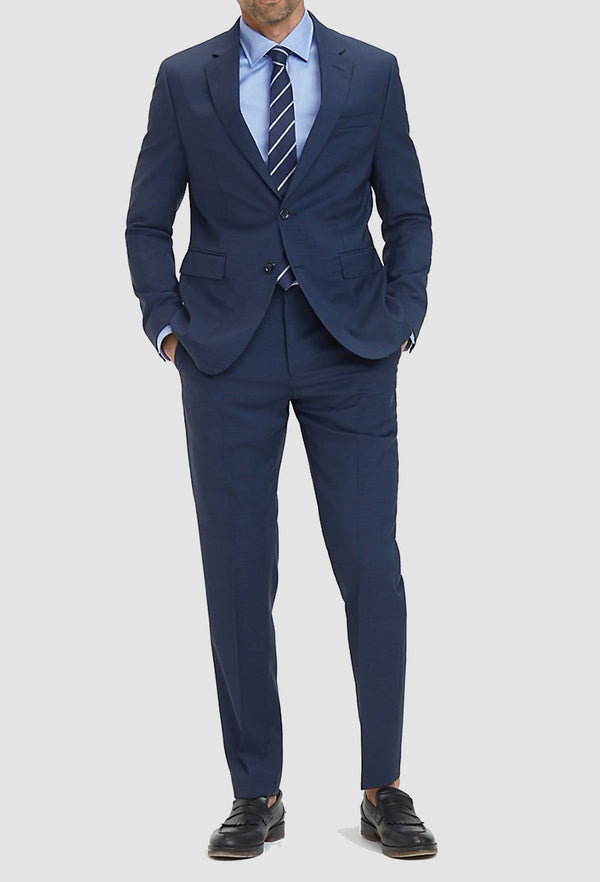 a model faces the front wearing the Tommy Hilfiger slim fit virgin wool suit in navy with a blue shirt and tie