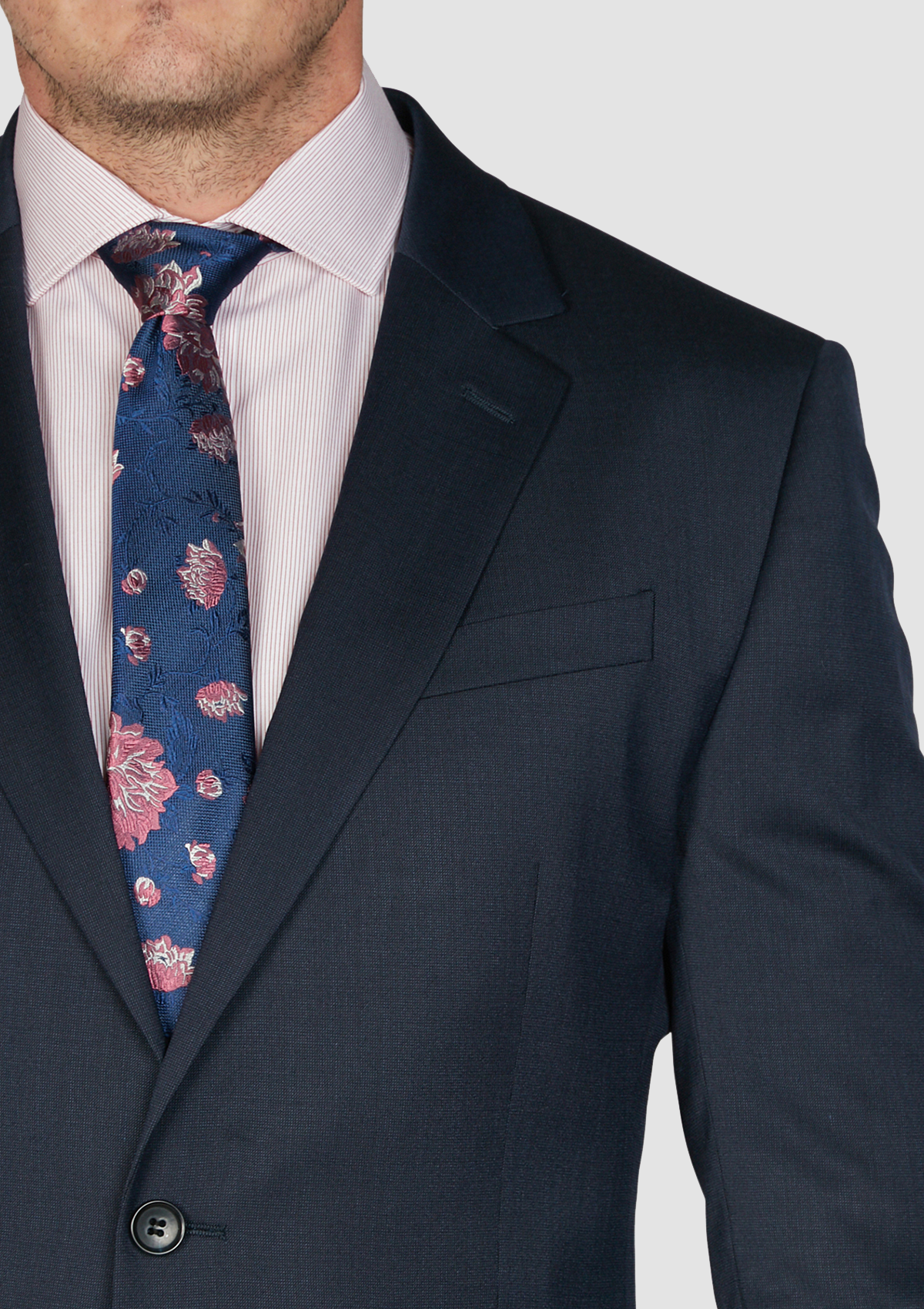 a man in a dark navy blue suit with a light coloured shirt and floral tie styled with it