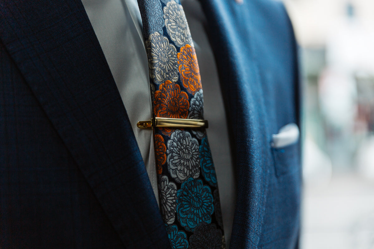 a navy suit with a printed tie and gold tie clip showing the details of products at mens suit warehouse