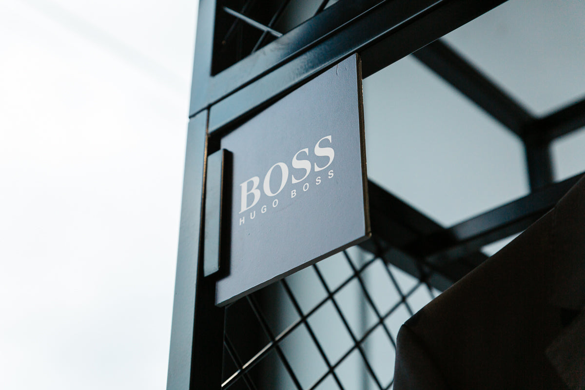 the hugo boss signs, a black square sign with the hugo boss logo printed on it attached to a black metal rack in store at mens suit warehouse