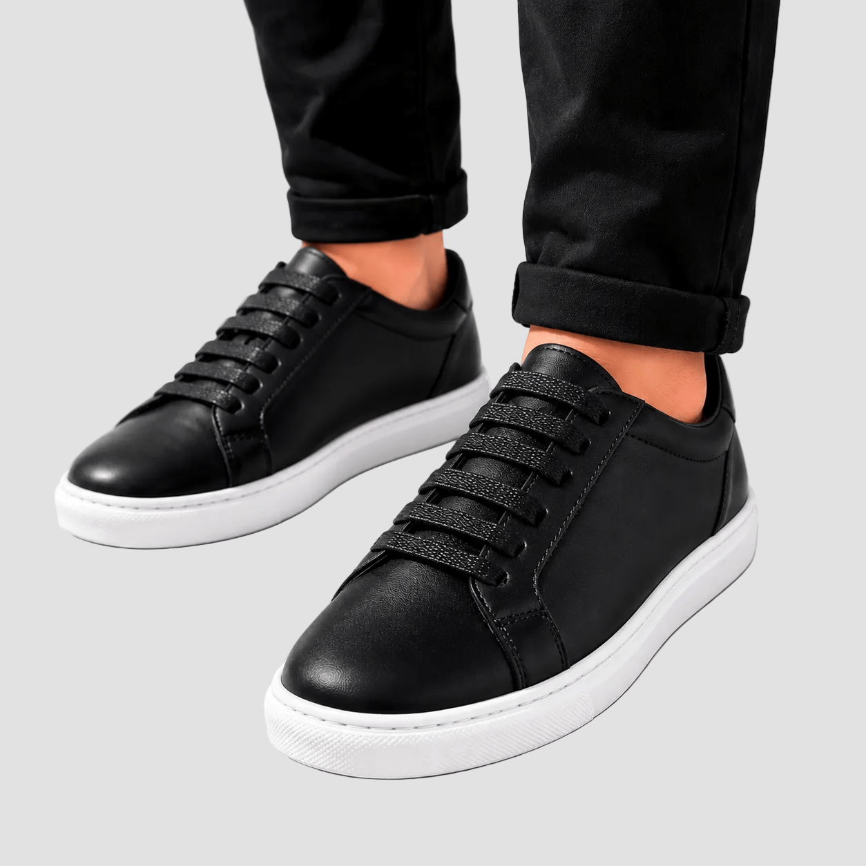 Black sneakers with white soles worn by a person on a light gray background