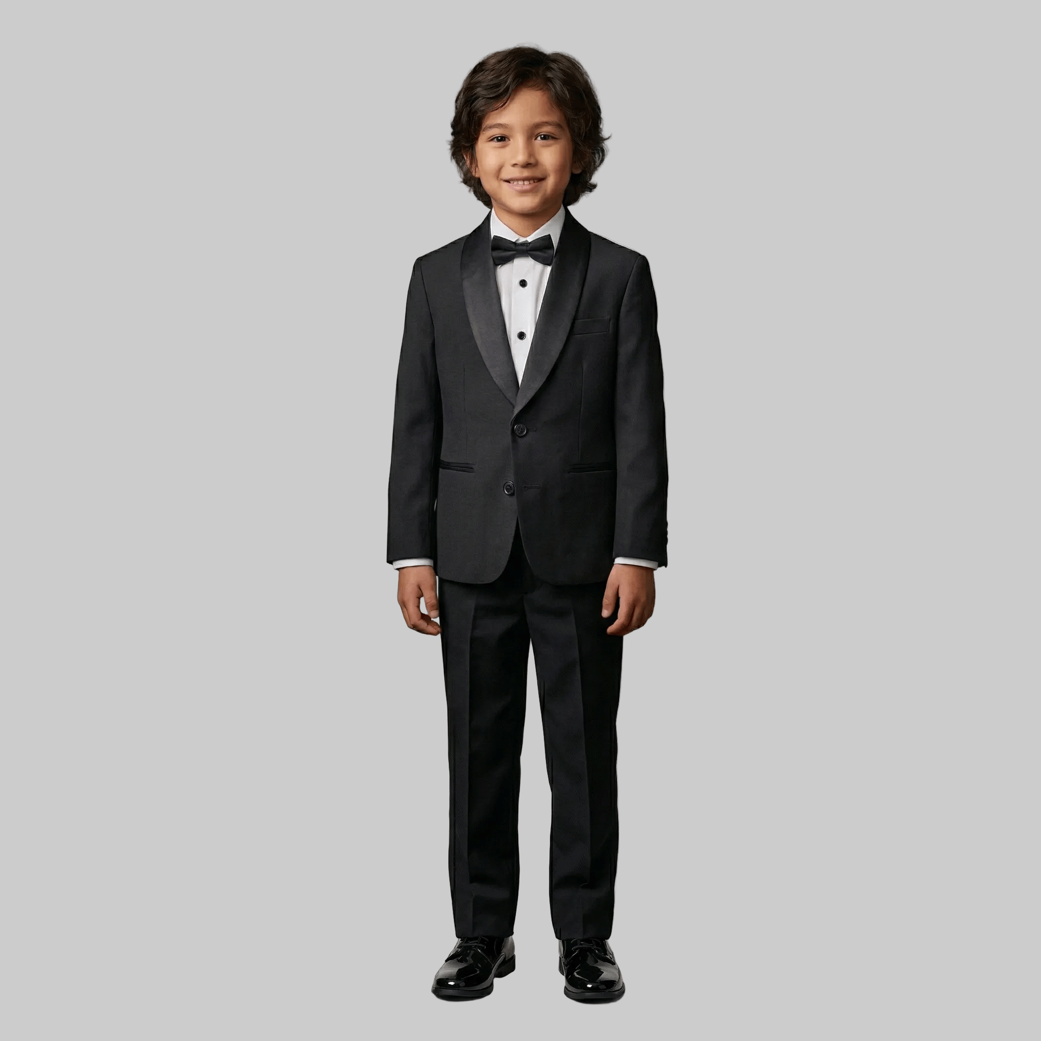 Young boy wearing a black tuxedo with a white shirt and black bow tie on a white background