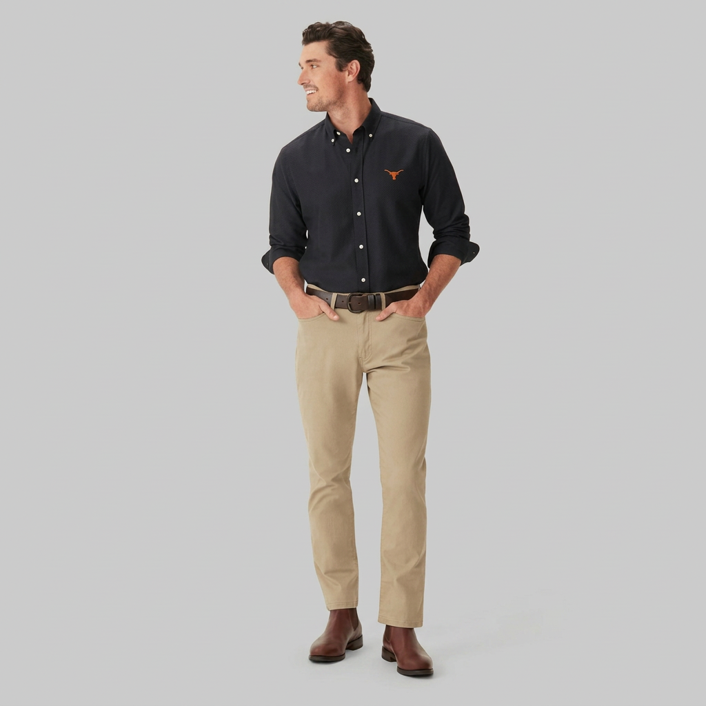A man modeling a black long-sleeve button-down shirt with a small red embroidered logo on the chest, paired with khaki trousers and brown leather shoes, against a solid light beige background.