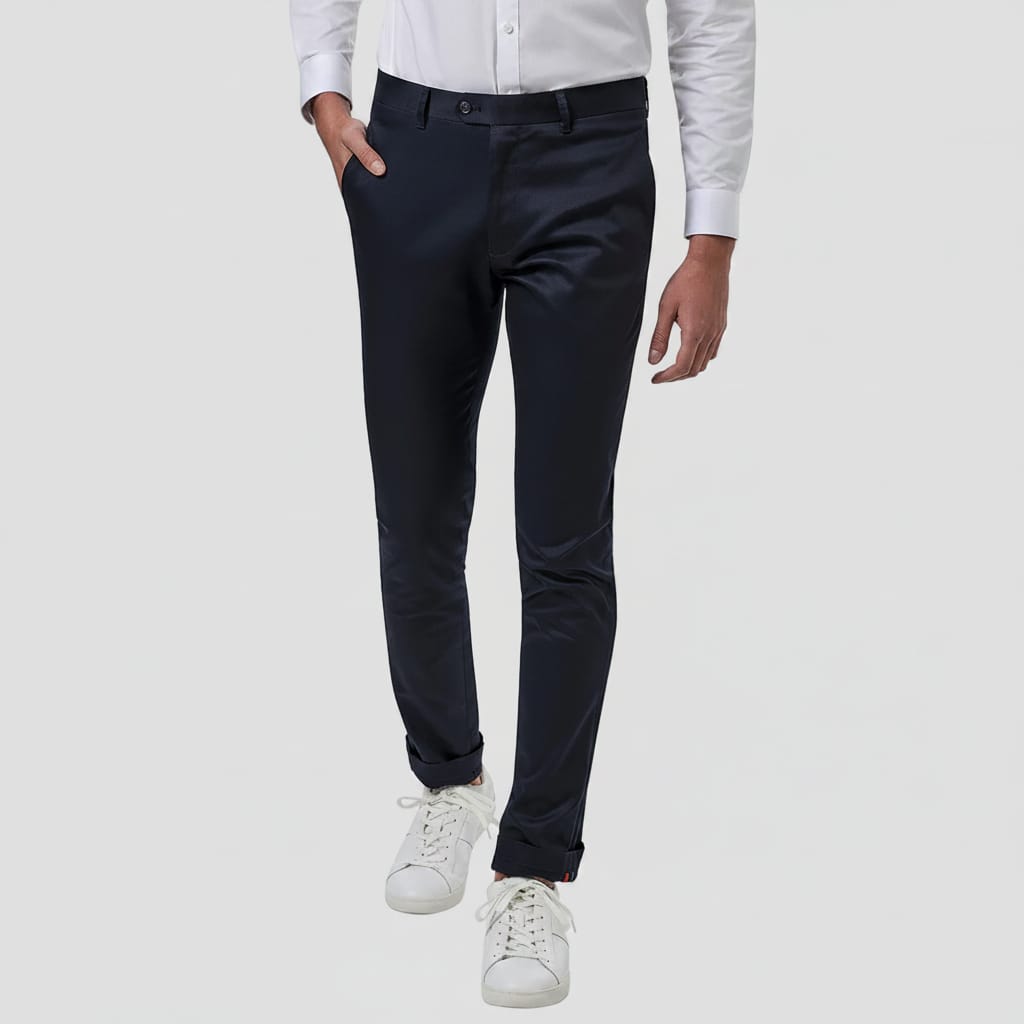 A person wearing slim-fit navy trousers, a white dress shirt, and white sneakers, shown from the waist down against a plain white studio background.