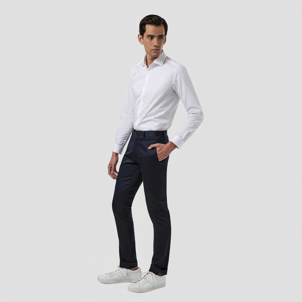A man modeling a white long-sleeve dress shirt and dark navy trousers, paired with white sneakers, against a solid white background.