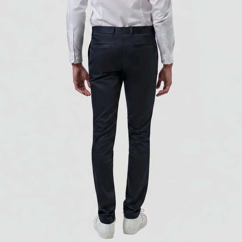 Rear view of a person wearing slim-fit navy trousers, a white dress shirt, and white sneakers against a plain white background.