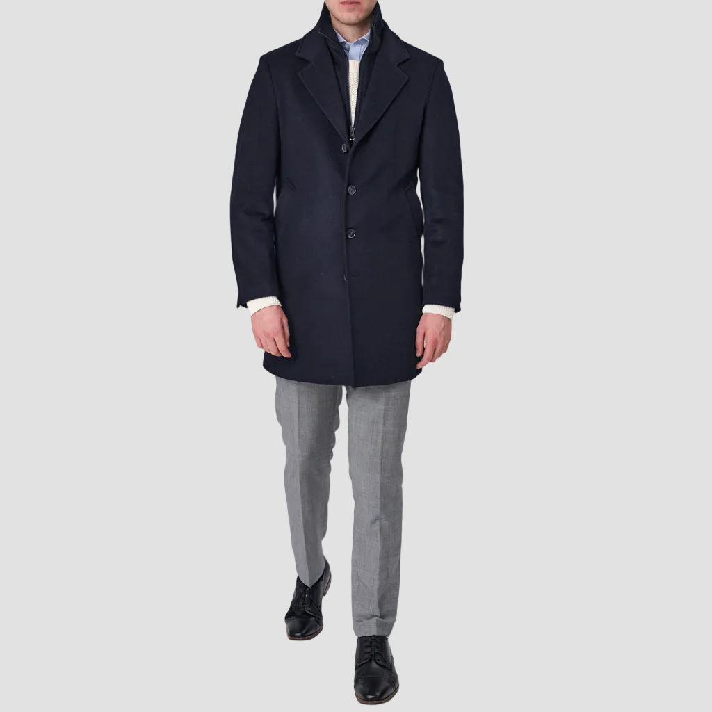 A navy blue, single-breasted, four-button front Savile Row coat with a removable collar, pictured on a male model.