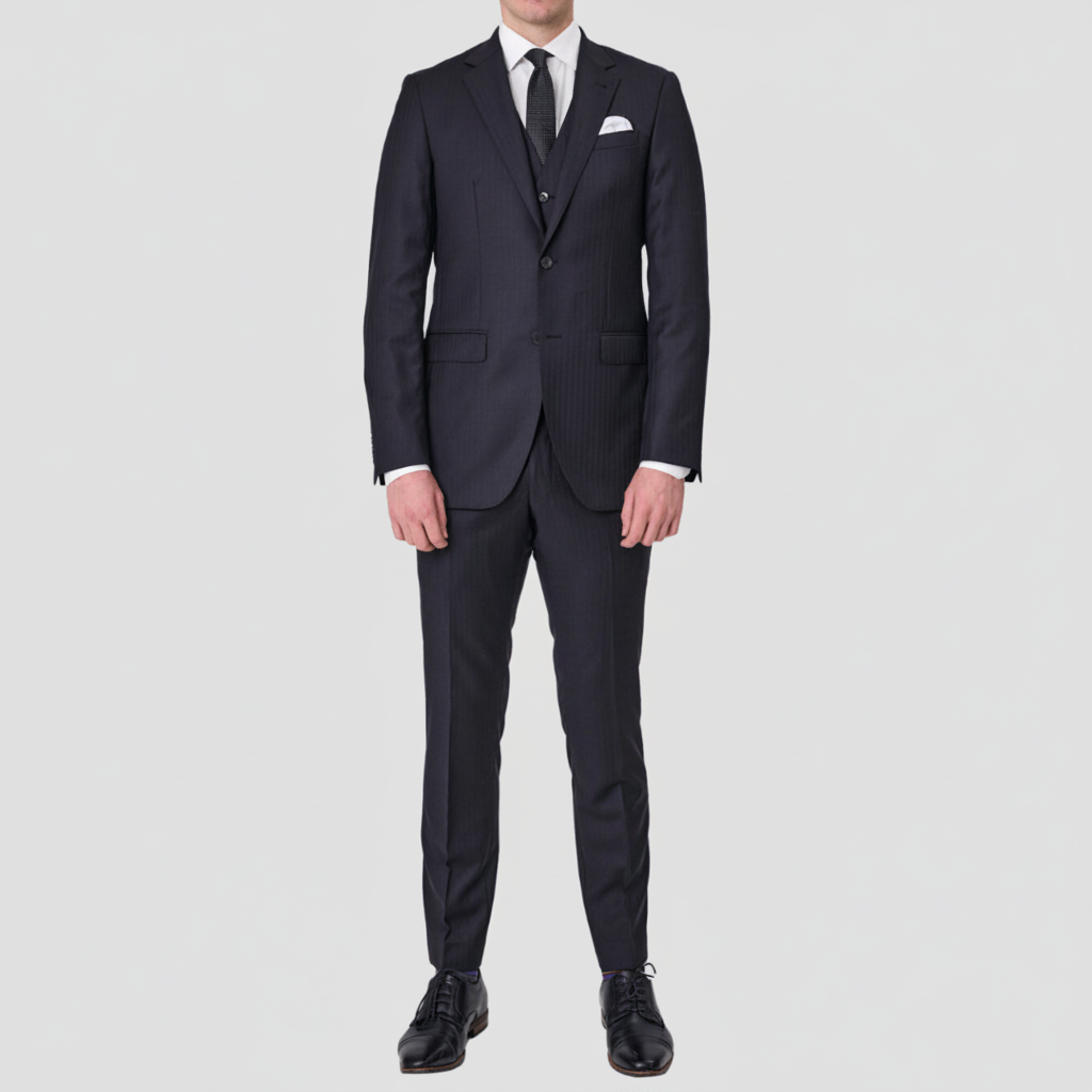 A man wearing a black tailored fit Abram Tasmanian Wool suit with a peak lapel, two button front, chest pocket, and front pockets, with matching trousers, vest, a white shirt and pocket square.