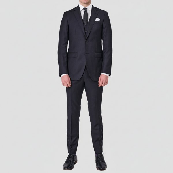A man wearing a black tailored fit Abram Tasmanian Wool suit with a peak lapel, two button front, chest pocket, and front pockets, with matching trousers, vest, a white shirt and pocket square.