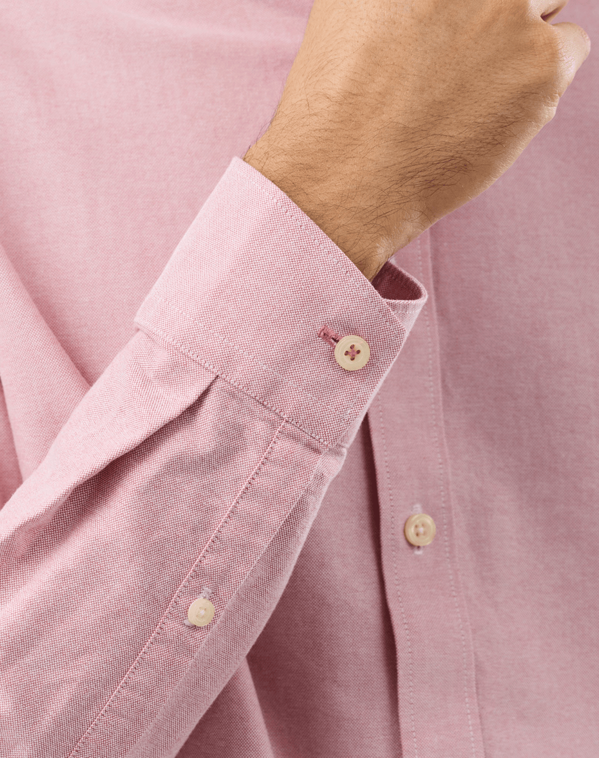 Close-up of a person wearing a light pink long-sleeve button-down shirt, showing the folded cuff with a button and the fabric texture.