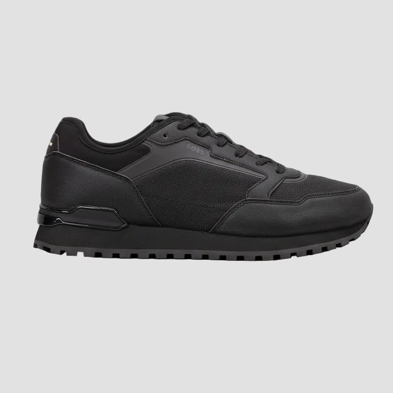 A black BOSS sneaker with a textured mesh and synthetic panel design, featuring black laces and a chunky black sole, shown from a side profile view on a white background.