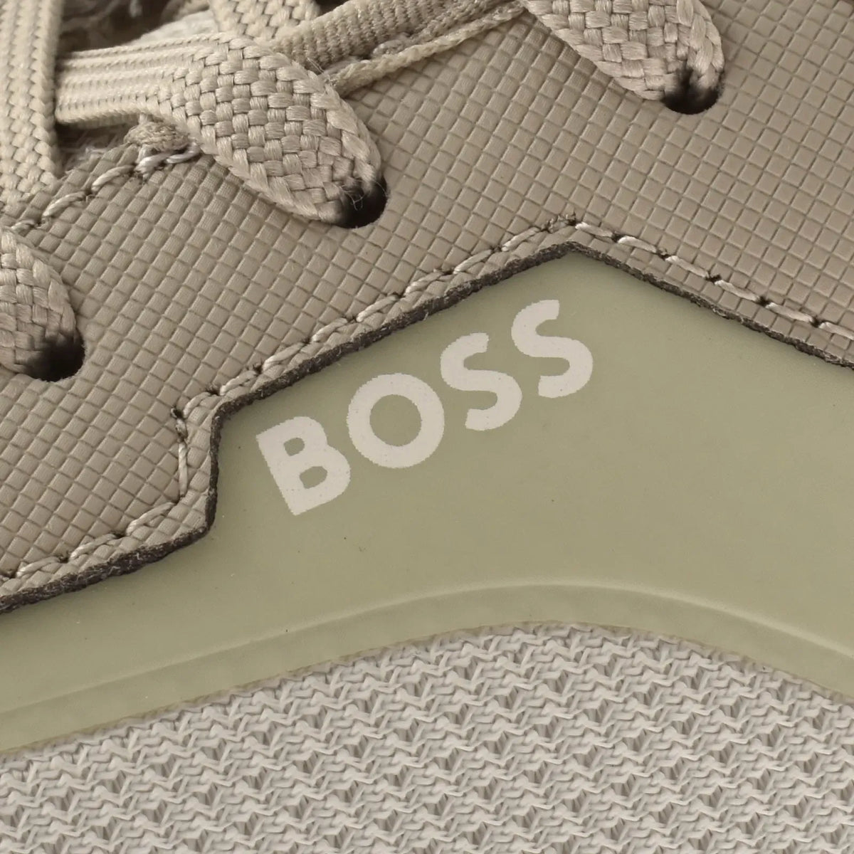Close-up of a BOSS sneaker showing the textured light gray upper, white BOSS branding on a pale green panel, and part of the woven laces.