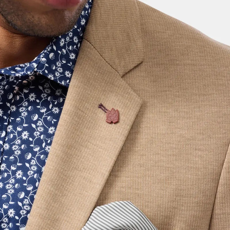 Close-up of a man wearing a beige textured blazer over a navy blue floral dress shirt, featuring a small pinkish-brown leather pocket square and a striped pocket square in the breast pocket.