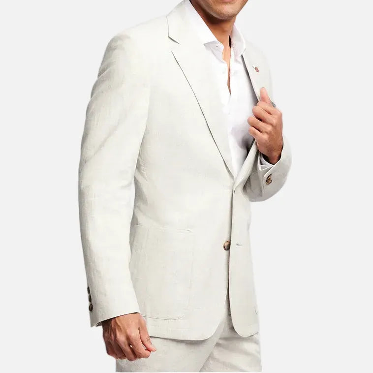 A smiling man wearing a light beige linen blazer and matching trousers over a white dress shirt, posed against a solid light gray background.