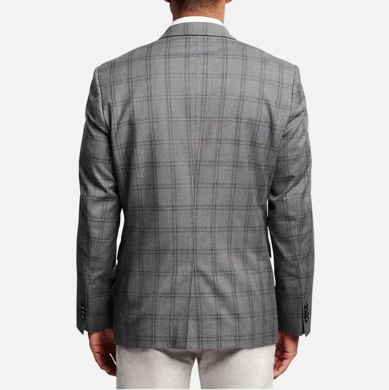 A man viewed from the back wearing a gray plaid blazer over a white collared shirt and white trousers, set against a plain light gray studio background.