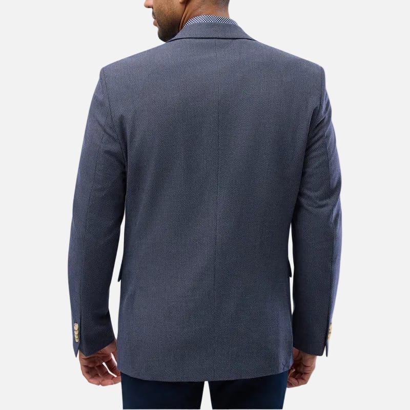 A man shown from the back wearing a textured navy blue blazer over a light blue collared shirt, set against a plain light gray background.