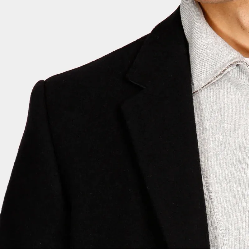 Close-up of a person wearing a black blazer over a light gray knit polo shirt, cropped from the lower face to the torso against a plain light background.