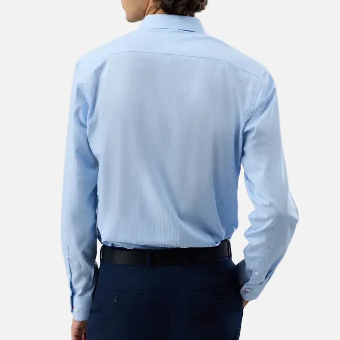A man shown from the back wearing a light blue long-sleeve dress shirt and dark navy trousers, photographed against a plain light gray studio background.