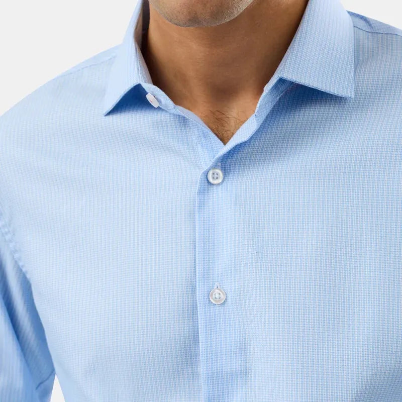 A close-up of a man wearing a light blue micro-check patterned dress shirt, showing the collar, front buttons, and chest area.