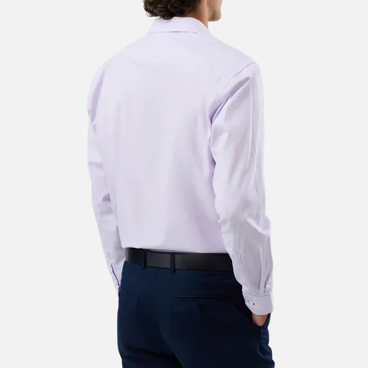 A man viewed from behind wearing a light lavender long-sleeve dress shirt, navy trousers, and a black belt, set against a plain light gray studio background.