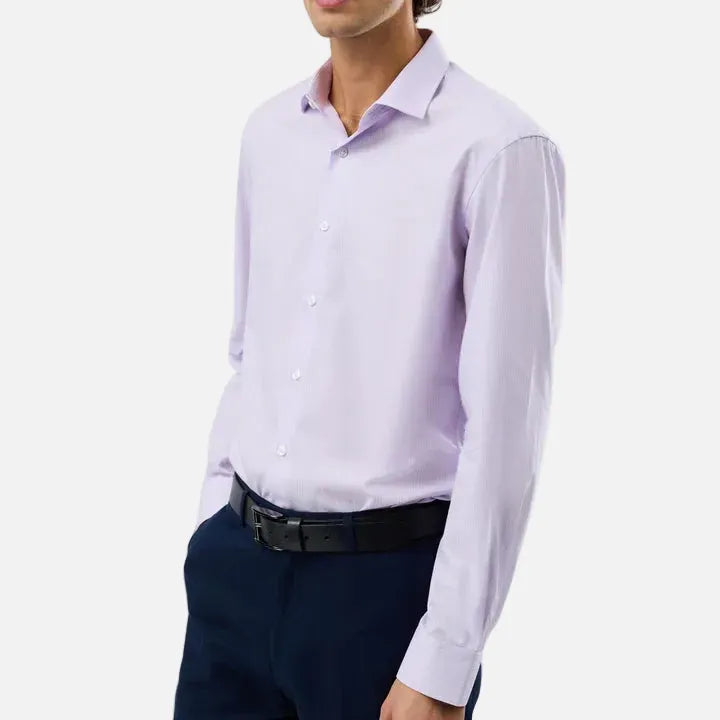 A man wearing a light lavender long-sleeve button-down dress shirt, dark navy trousers, and a black belt, photographed against a plain light gray studio background.