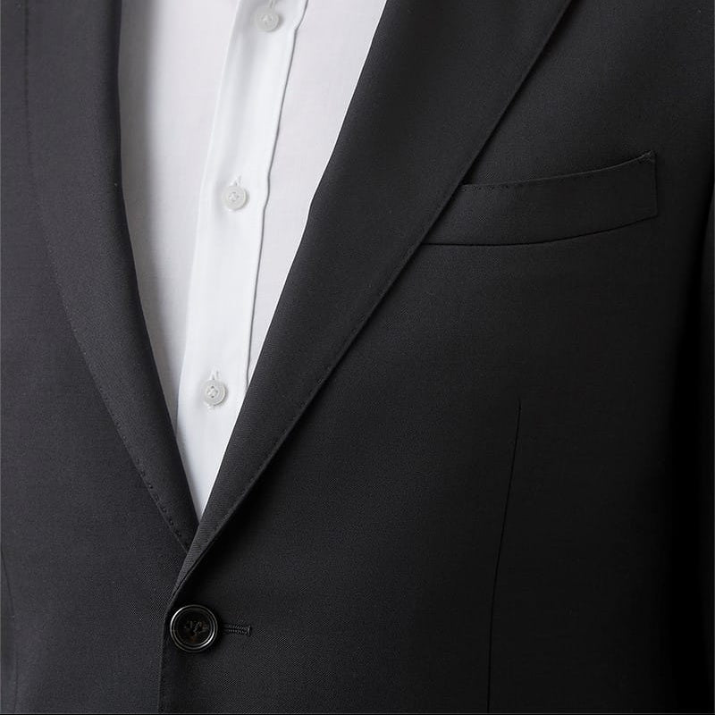A close-up of a man wearing a black suit jacket over a white dress shirt, with a small circular lapel pin visible on the jacket.